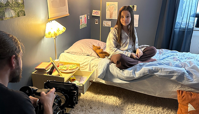Alma sitter i en säng och blir filmad av en kameraman.